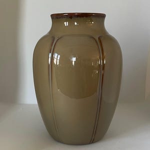 Puede incluir: Un jarr&oacute;n de cer&aacute;mica marr&oacute;n con un acabado brillante y l&iacute;neas verticales. El jarr&oacute;n tiene un cuerpo redondeado y una abertura ligeramente acampanada.