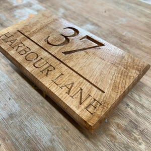 May include: Wooden address sign with the number 37 and the words "HARBOUR LANE" carved into the surface. The sign is rectangular and made of light brown wood.