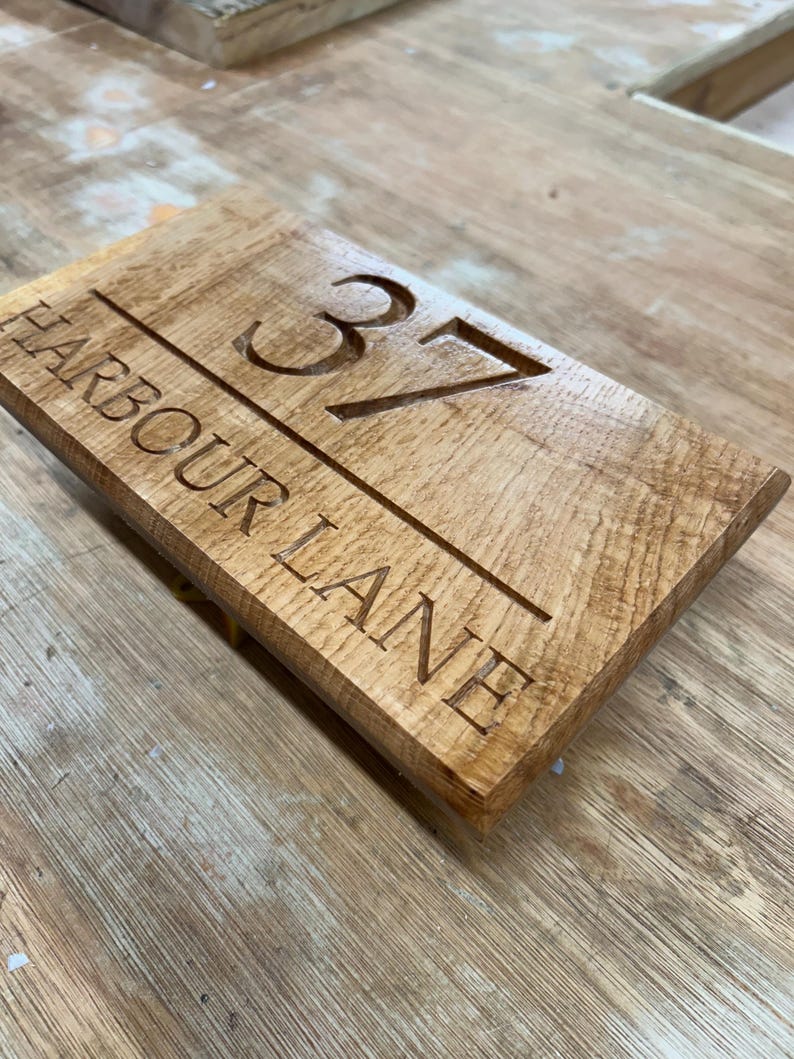 May include: Wooden address sign with the number 37 and the words "HARBOUR LANE" carved into the surface. The sign is rectangular and made of light brown wood.