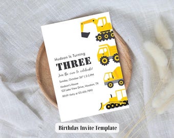 May include: A white birthday invitation template with yellow construction vehicles. The text reads "Hudson Is Turning THREE" with event details. The invitation is on a wooden plate with a white cloth and decorative elements.