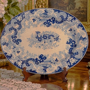 May include: An oval ceramic serving platter featuring a blue and white transferware pattern. The design displays intricate floral motifs, swirling scrollwork, and architectural elements reminiscent of traditional pagoda landscapes.
