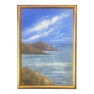 May include: An oil painting of a coastal landscape with a gold frame. The artwork depicts a blue sky with white clouds and several birds in flight. The scene includes a body of water, hills, and a shoreline.