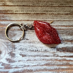 Könnte beinhalten: Ein roter Glitzer-Lippen-Schlüsselanhänger mit einem silbernen Metallring und einer Kette.