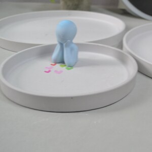 Pu&ograve; includere: Un piatto in ceramica bianca con una statuetta azzurra di una persona seduta con la testa tra le mani. Il piatto &egrave; decorato con piccoli cuori colorati.