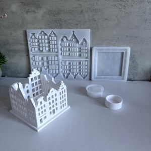 May include: White plastic mold for making a miniature house with a square base and a design of a row of houses with windows. The mold is shown with a finished miniature house made from the mold.