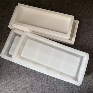 May include: Three white silicone moulds for making rectangular soap bars. The moulds are stacked on top of each other.