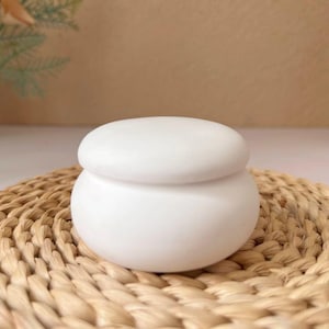 Op de afbeelding: Een witte keramische pot met een deksel. De pot heeft een ronde vorm en een gladde, matte afwerking.