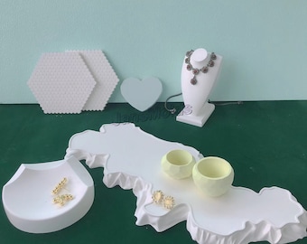May include: White ceramic display stand with a heart-shaped cutout, two small bowls, and a necklace stand. The stand is shaped like a stylized island with a jagged coastline. The stand is on a green surface.