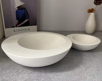 May include: Two white ceramic bowls, one larger than the other, are displayed on a gray surface. The larger bowl has a wide, shallow rim and a rounded bottom. The smaller bowl is similar in shape but smaller in size.