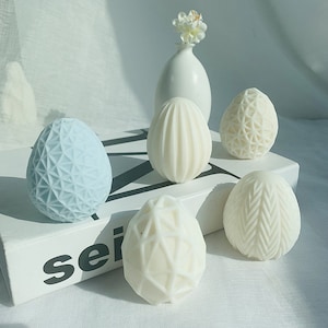 Könnte beinhalten: Fünf dekorative Eier, jedes mit einem anderen Muster. Die Eier sind weiß und blau und auf einer weißen Oberfläche angeordnet. Die Eier sind aus einem glatten, harten Material gefertigt.