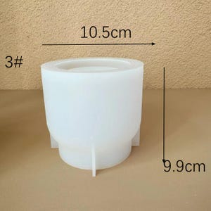 以下が含まれることがあります： コンクリート製のプランターを作るための白いシリコンモールド。モールドは幅10.5cm、高さ9.9cmです。モールドは丸いトップと3本の脚が付いたベースを持っています。