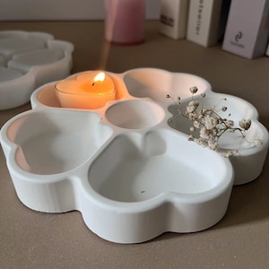 May include: White ceramic tray shaped like a paw print with five heart-shaped indentations. A small tea light candle is burning in one of the indentations. Dried white flowers are placed in another indentation.