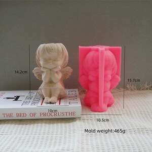 Op de afbeelding: Een roze siliconen mal voor een engelbeeldje. De mal is 15,7 cm hoog, 10,5 cm breed en weegt 465 gram. De mal wordt getoond naast een afgewerkt engelbeeldje.