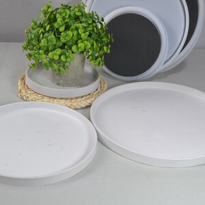 Pu&ograve; includere: Tre vassoi rotondi in ceramica bianca di diverse dimensioni, con una piccola pianta verde in un vaso bianco sul vassoio pi&ugrave; piccolo. I vassoi sono impilati uno sopra l'altro.