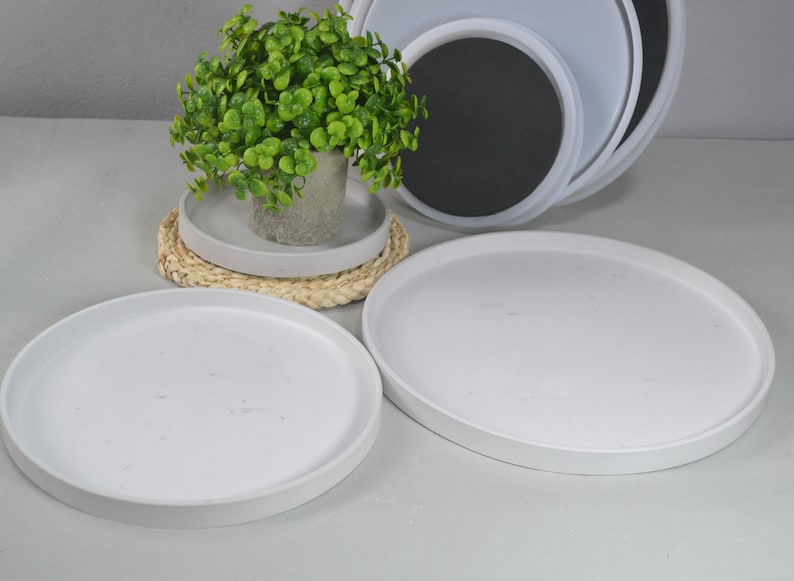 Pu&ograve; includere: Tre vassoi rotondi in ceramica bianca di diverse dimensioni, con una piccola pianta verde in un vaso bianco sul vassoio pi&ugrave; piccolo. I vassoi sono impilati uno sopra l'altro.