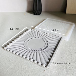May include: Grey silicone mould with a circular design and a scalloped edge. The mould measures 14.9 cm by 14.9 cm and is 1.4 cm thick.