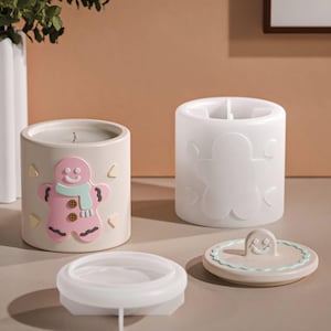 Può includere: Una candela beige con un design a forma di omino di pan di zenzero rosa, uno stampo per candele bianco, un coperchio trasparente e un coperchio beige con un omino di pan di zenzero sorridente.