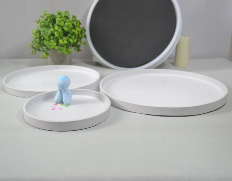 Pu&ograve; includere: Tre vassoi in ceramica bianca di diverse dimensioni, con il vassoio pi&ugrave; piccolo che presenta una piccola figurina blu. La figurina &egrave; seduta sul vassoio con le mani giunte davanti al viso.