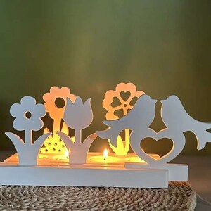 Könnte beinhalten: Weißer Kerzenhalter aus Holz mit floralem und Vogelmotiv. Der Halter hat fünf Kerzenplätze und ist perfekt, um jedem Wohndesign einen Hauch von Verspieltheit zu verleihen.