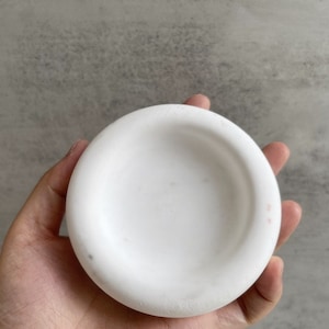 以下が含まれることがあります： 縁が高く、白い陶器のボウル。ボウルは滑らかで、わずかにざらざらした表面をしています。