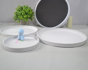 May include: Three white ceramic trays of varying sizes, with a small blue figurine sitting on the smallest tray. The figurine is holding its hands together in front of its face. There are small colorful hearts scattered around the figurine.