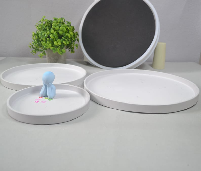 Pu&ograve; includere: Tre vassoi in ceramica bianca di diverse dimensioni, con una piccola statuina blu seduta sul vassoio pi&ugrave; piccolo. La statuina tiene le mani giunte davanti al viso. Ci sono piccoli cuori colorati sparsi intorno alla statuina.