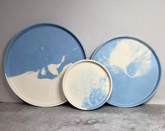 May include: Three round, blue and white, resin trays with a marbled design. The trays are nested together, with the largest tray at the bottom and the smallest tray at the top.