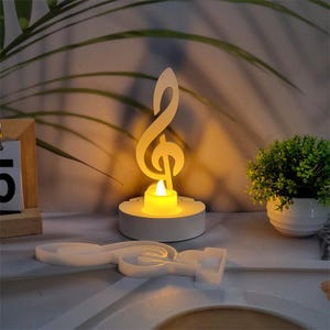 Op de afbeelding: Witte kaarsenhouder in de vorm van een vioolsleutel met een kleine, brandende kaars erin. De kaarsenhouder staat op een wit oppervlak.