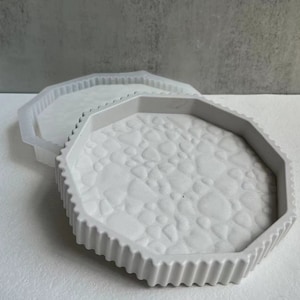 Puede incluir: Una bandeja octogonal blanca con un diseño de guijarros texturizado en relieve. La bandeja tiene un borde blanco liso.
