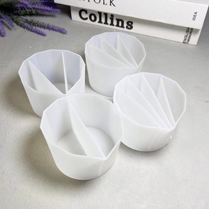 May include: Four white plastic containers with dividers. Each container has a circular base and a cylindrical shape. The containers are designed to hold small items, such as pens, pencils, or makeup brushes.