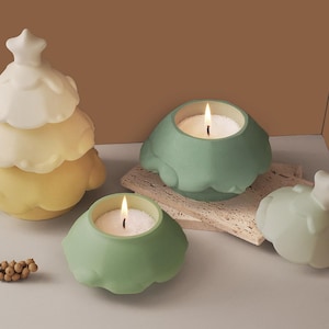 Può includere: Tre portacandele in ceramica a forma di albero di Natale. Due sono verdi e uno è bianco e giallo. Le candele sono accese e le fiamme sono visibili.