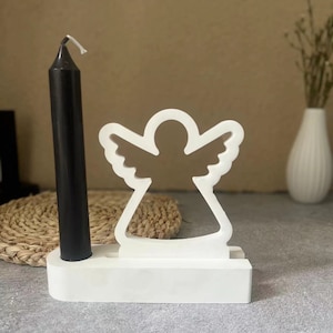 May include: White wooden candle holder shaped like an angel with a black candle in the centre.