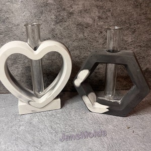 May include: Two concrete vases with glass test tubes. One vase is heart-shaped and the other is hexagonal. Both vases are painted in a black and white marbled pattern.