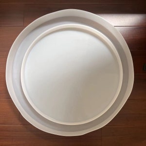 Op de afbeelding: Een ronde witte serveerschaal met een kleinere ronde witte schaal erin. De schalen zijn in elkaar genest.