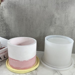Pode incluir: Dois moldes de silicone para fazer vasos de cimento. O molde à esquerda é um design de dois tons com a parte superior branca e a inferior rosa. O molde à direita é de uma única cor branca.