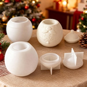 May include: A selection of white ceramic candle holders and moulds. The candle holders are spherical with a circular opening at the top. One has a Christmas tree design. The moulds are white and for candle making.