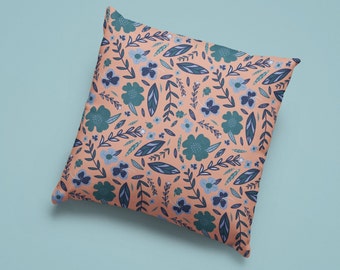 Puede incluir: Una almohada de color melocotón con un patrón floral con flores y hojas azules y verdes.