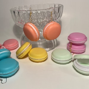 May include: A set of colorful macaron-shaped earrings. The earrings are made of plastic and have a gold chain. The macarons are in shades of pink, blue, yellow, and green.