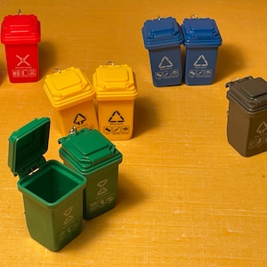 Puede incluir: Un conjunto de diez cubos de basura en miniatura de varios colores, incluyendo rojo, amarillo, azul y gris. Cada cubo tiene un símbolo de reciclaje diferente, incluyendo un triángulo de reciclaje, una X y un árbol.