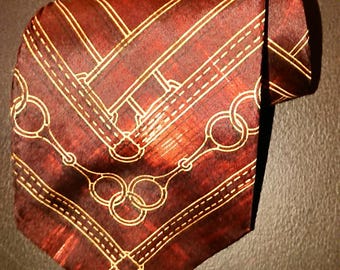 Könnte beinhalten: Eine weinrote Krawatte mit einem sich wiederholenden Muster aus goldenen Reithalftern und Nähten. Die Krawatte ist gefaltet und zeigt das Design. Der Stoff hat eine subtile Textur, für einen klassischen und eleganten Look.