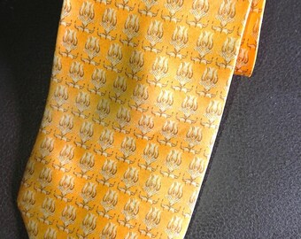 Könnte beinhalten: Eine gelbe Krawatte mit einem sich wiederholenden Muster aus stilisierten floralen Designs in einem helleren Gelb- und Braunton. Die Krawatte ist gefaltet und liegt auf einer dunklen Oberfläche, die ihr detailliertes Design und ihre Farbe hervorhebt.