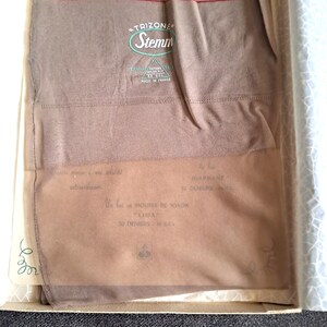 Peut inclure: Bas en nylon vintage dans une boîte. Les bas sont de couleur marron clair et pliés à l'intérieur de la boîte. La boîte porte la marque "Stemm" et "TRIZONE", ainsi que d'autres textes. Fabriqué en France.
