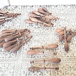 May include: A collection of antique wooden lace bobbins, featuring a variety of shapes and sizes. The bobbins are a warm brown color, with some showing signs of age and use. They are arranged on a white lace tablecloth.