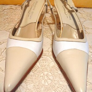 May include: A pair of cream-colored slingback heels with pointed toes. The shoes feature a white band across the vamp and a small heel. The brand name "ELIZABETH STUART" is visible on the insole. The shoes are displayed on a lace surface.