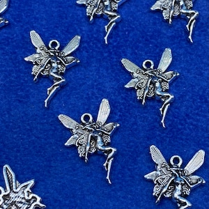 Puede incluir: Encantos de hadas plateadas con alas detalladas y atuendo fluido sobre un fondo azul. Cada dije tiene un lazo en la parte superior para sujetarlo a joyas o manualidades. Los dijes miden aproximadamente 2,5 cm de altura.