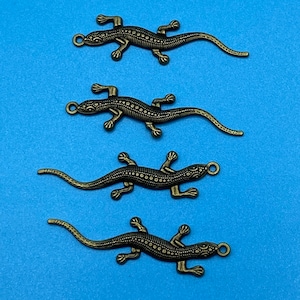 Peut inclure: Quatre breloques de lézard de couleur or antique avec une surface texturée. Les lézards sont en rang, face au côté droit de l'image.