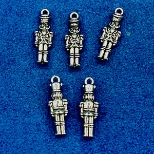 Puede incluir: Cinco dijes de cascanueces plateados con un diseño detallado. Los dijes tienen un bucle en la parte superior para colgar.