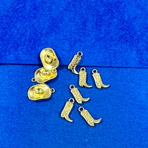 May include: Gold-colored charms in the shape of cowboy hats and cowboy boots. The charms are small and detailed, with a loop at the top for attaching to jewelry or other crafts. The charms are arranged on a blue surface.