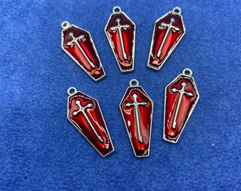 Op de afbeelding: Zes zilverkleurige kistcharms met een rode emaille afwerking en een zilveren kruisontwerp.