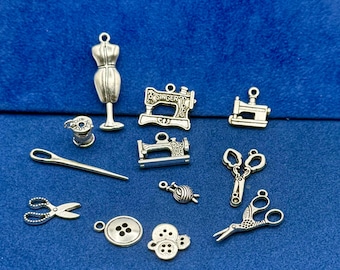 May include: A selection of silver sewing charms, including a dress form, sewing machines, scissors, a needle, thread spool, buttons, and a ball of yarn. The charms are displayed on a blue background.
